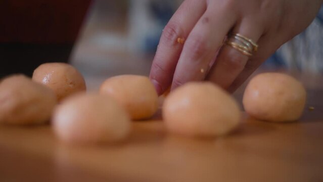 Close up of small traditional Brazilian cheese buns lying on the wooden table in the kitchen. Slow motion, shallow depth of field.  