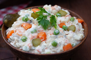Bowl of russian salad olivier with meat and vegetables on a wooden table. Popular food for New Year and Christmas.