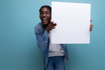 American man with dreadlocks in a denim jacket demonstrates a paper poster with a mockup