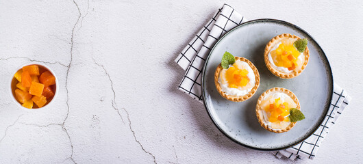 Appetizing tartlet with whipped cream, canned fruit and mint on a plate top view web banner