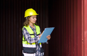 Young caucasian woman dressed in yellow hardhat and safety vest examine inside a cargo container panel while holding a clipboard.