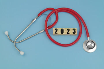 Medicine and health care in year 2023. Red stethoscope and numbers  2023 on wooden cubes on blue background. 