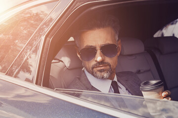Confident mature businessman enjoying coffee while looking through a car window