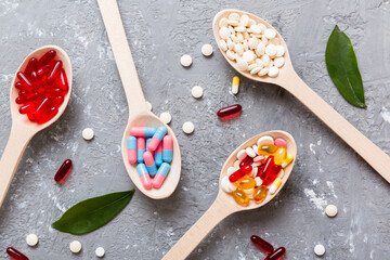 Vitamin capsules in a spoon on a colored background. Pills served as a healthy meal. Red soft gel vitamin supplement capsules on spoon