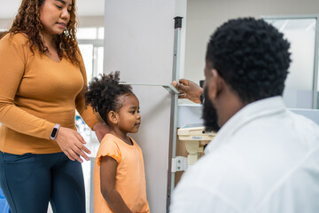 Mature doctor measuring black African little girls height in hospital. 