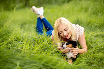 Fototapeta premium A beautiful girl with a dog sits in the park on the grass. Love to the animals. Home pet on a walk. Animal protection. Bernese mountain dog puppy.