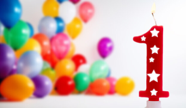 Number 1 birthday celebration candle against a bright white background with colorful balloons , burning party candle for one year old. Happy Birthday concept