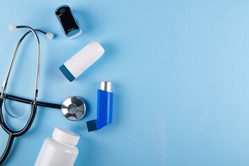Top view of stethoscope, oximeter, bottle of pills and inhalers on blue background with copy space....