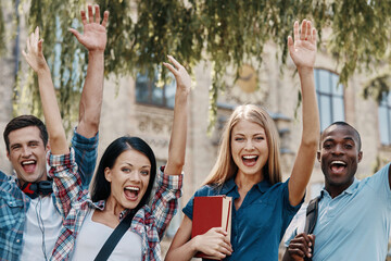 Group of happy students gesturing while standing in front of University building together