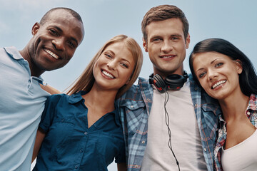 Low angle view of happy young people embracing and smiling with blue sky in the background