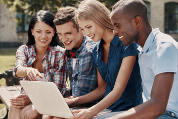 Group of happy students using laptop while spending time outdoors together