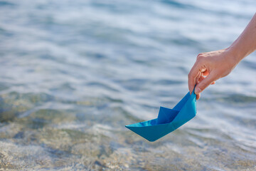 Obraz premium hands of a young woman with a paper boat by the sea in summertime