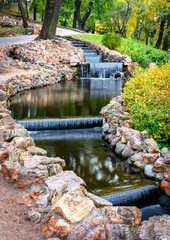 Stones bordered stream and small artificial waterfalls at Bastion Hill park in autumn city park at Riga, Latvia.