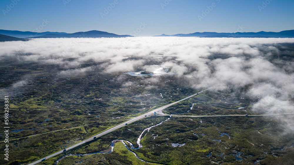 Wall mural Aerial view of a road running through a deserted valley with low cloud and fog above (Glen Coe, Scotland) - Wall murals