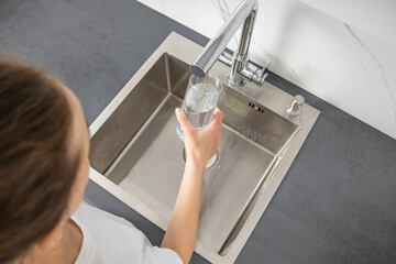 Woman pouring water into glass in kitchen. Top view, flat lay