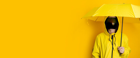 Young woman in a mask of cyberpunk goggles in a yellow jacket under a yellow umbrella on a yellow...