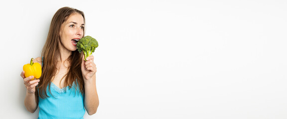 Fototapeta na wymiar Young woman biting fresh broccoli holding paprika on white background. Banner