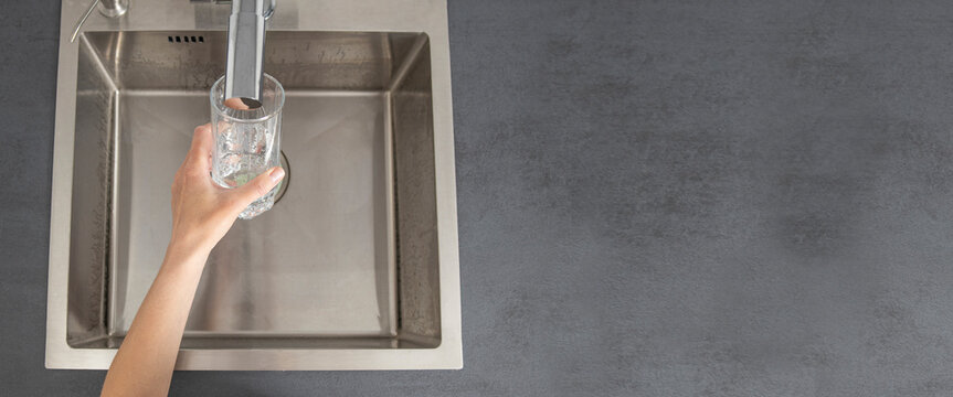 Woman's hand holding a glass pours water from a faucet in the kitchen. Top view, flat lay