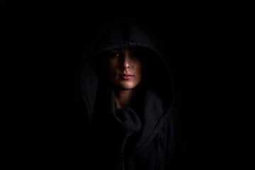 Young woman in a black hood on a black background - obrazy, fototapety, plakaty