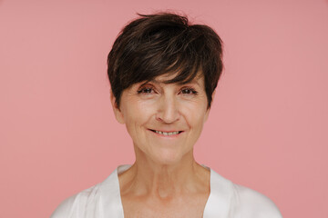 Senior woman smiling at camera while standing isolated over pink background