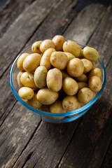 New or baby raw potatoes in a glass bowl set on a wooden background, no people