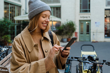 Smiling woman using smartphone standing with bike outdoors
