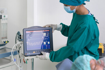 Multi-parameter patient monitor in operating room, controlled by nurse in surgical green gown...