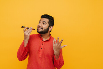 Indian man sending voice message using smartphone isolated over yellow background