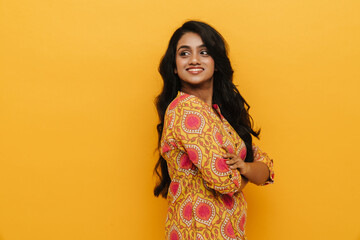 Young indian woman smiling while standing with folded arms isolated over yellow background