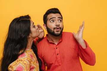 Indian couple gossiping isolated over yellow background