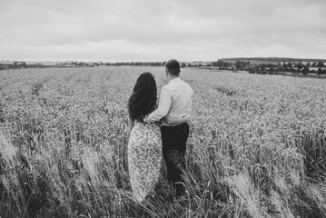 Man and woman embrace in nature. Loving couple hugs, walks enjoys glade. Family hugging in wheat field. Honeymoon trip. Weekend vacation holidays concept. Love story. Back view. Black and white photo.
