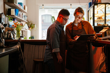 Woman teaching man with down syndrome how to use tablet during internship in cafe