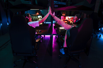 Gamers giving high five to each other while playing online game on tournament in cybersport club