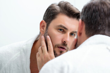 Middle aged hispanic man looking in mirror, facial skin and stubble. Male beauty care product....
