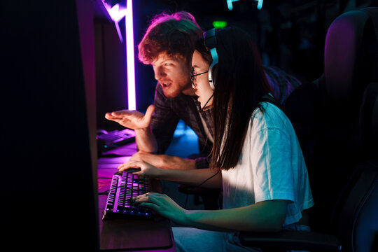 Friend of asian girl watching her playing video game and assisting her in cybersport club