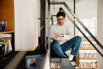 Fototapeta premium Young man student reading book while sitting in library