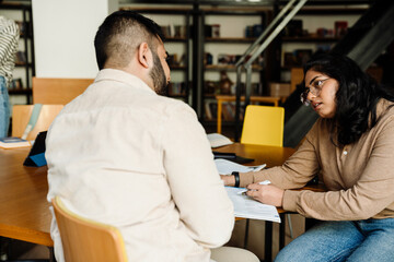 Indian woman explaining something to her сollege classmate while studying in library