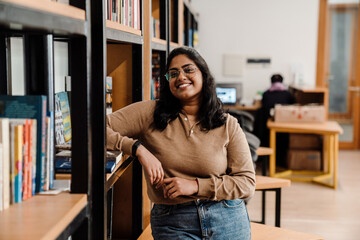 Indian woman student smiling at camera while standing in library