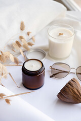 Soy wax aroma candle in brown jar on bed , with fashion glasses. Candle mockup design