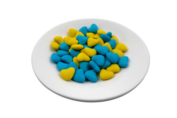 White plate with blue and yellow heart-shaped candies (close-up) isolated on white background. State symbols of Ukraine