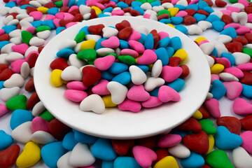 A white plate with multi-colored heart-shaped candies (close-up), against the background of the same multi-colored candies