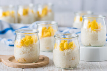Coconut rice pudding with mango in dessert glasses on white wooden background