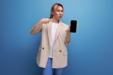 lucky blond young woman in a jacket with a gadget screen mockup in her hands on a studio background