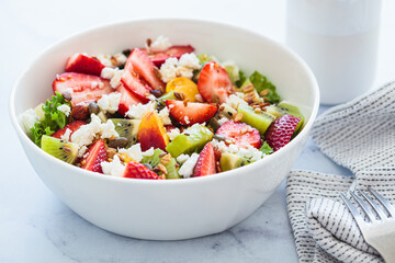 Fruit salad with feta and seeds in white bowl on white table. Healthy vegan detox summer recipe.
