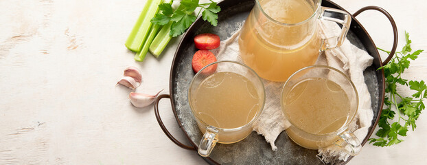 Glass jar with yellow fresh bone broth on white background. Healthy low-calories food is rich in vitamins, collagen and anti-inflammatory amino acids.