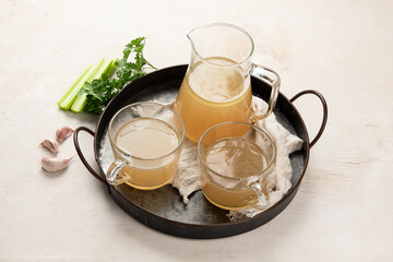 Glass jar with yellow fresh bone broth on white background. Healthy low-calories food is rich in vitamins, collagen and anti-inflammatory amino acids.