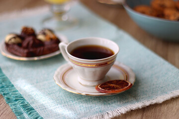 Plate of chocolate pralines, bowl of cookies, cups of tea, glasses of juice and lit candles on the table. Selective focus.