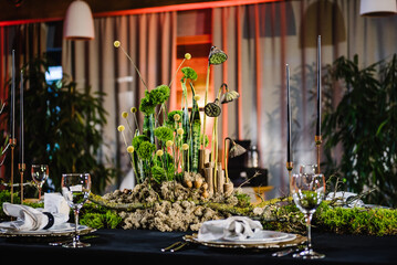 Wedding reception. Rustic. Composition of bark tree, wooden decor, moss in restaurant. Table decorated plates and glasses, candles, flowers, greenery. Interior of table for guests with natural decor.