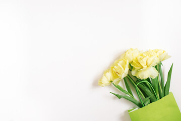 Beautiful yellow tulip flowers in a green paper bag with space for text. The concept of sales, spring discounts, shopping and environmentally friendly packaging.