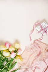 Women's clothing, gift box and tulip flowers. Minimalistic composition in pastel beige and pink tones. Top view, flat lay, copy space. The concept of a woman's birthday, fashion and blogging